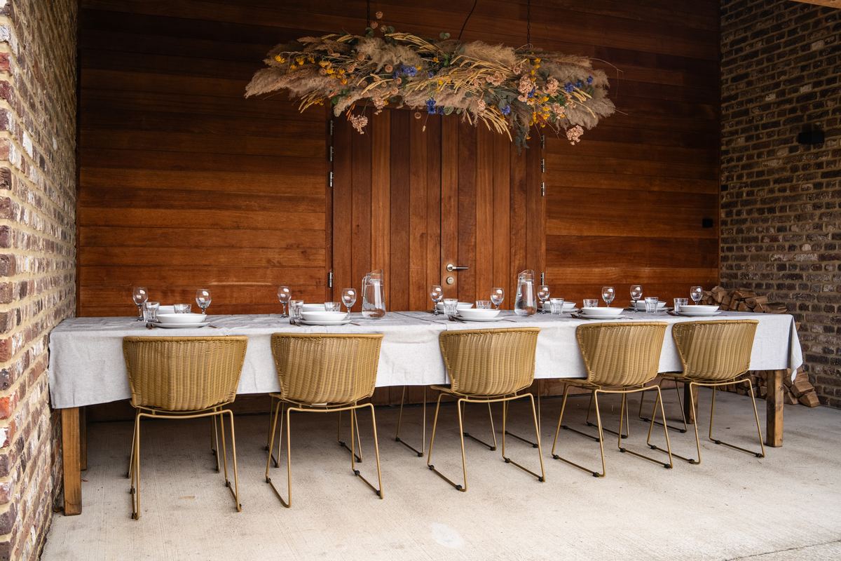 Lange gedekte eettafel voor veertien personen met gele stoelen onder een droogbloemenkroon