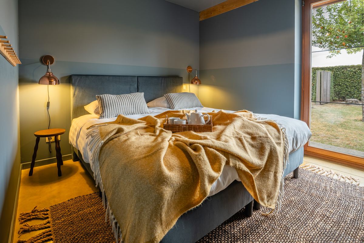 Slaapkamer met raam op de tuin, okergele plaid en ontbijtblad op bed